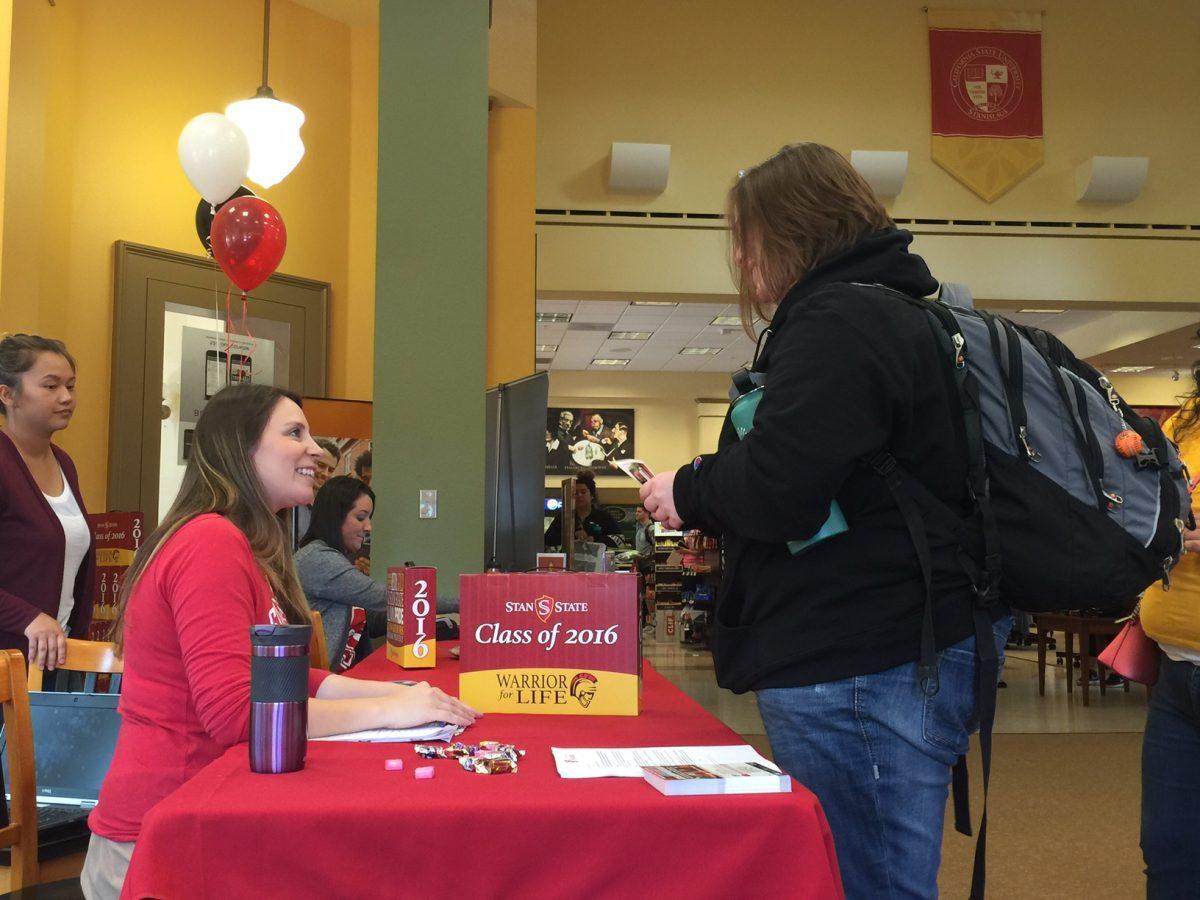 Alumni Association Grad Fair representative hands Stan State student her graduation package during Grad Fair at Stan State Bookstore on April 12.