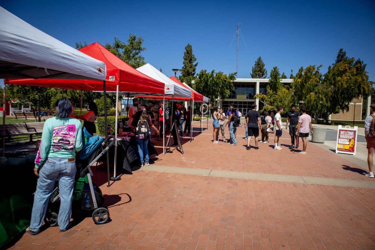 A row of student organization booths and students talking at the quad of Stanislaus State.