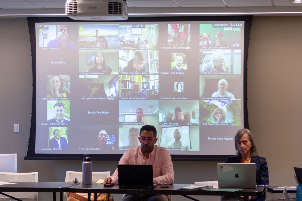 Senators of the Academic Senate hard at work with a projection of the Senators joining in virtually on the screen behind them.