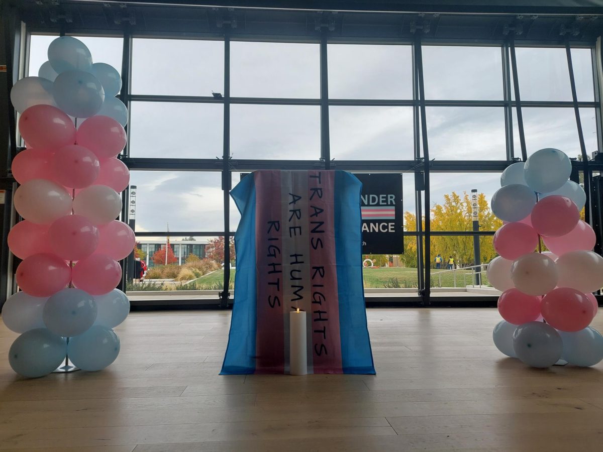 The podium in front of the Warrior Steps draped with a Trans Pride flag, reading "TRANS RIGHTS ARE HUMAN RIGHTS," alongside balloons to celebrate the lives of the deceased and candles to memorialize them.