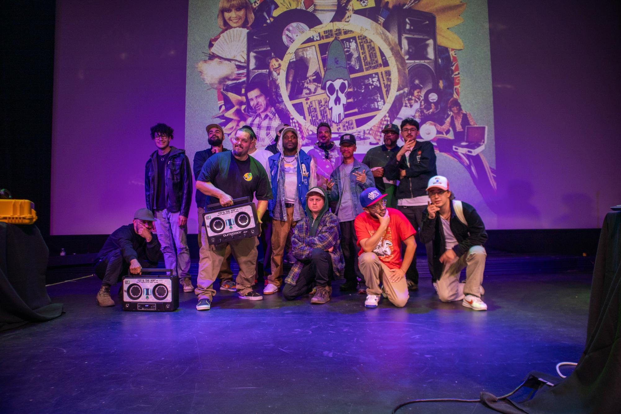 View of artists and emcees on stage at the Modesto State Theater, standing together posing and smiling. 