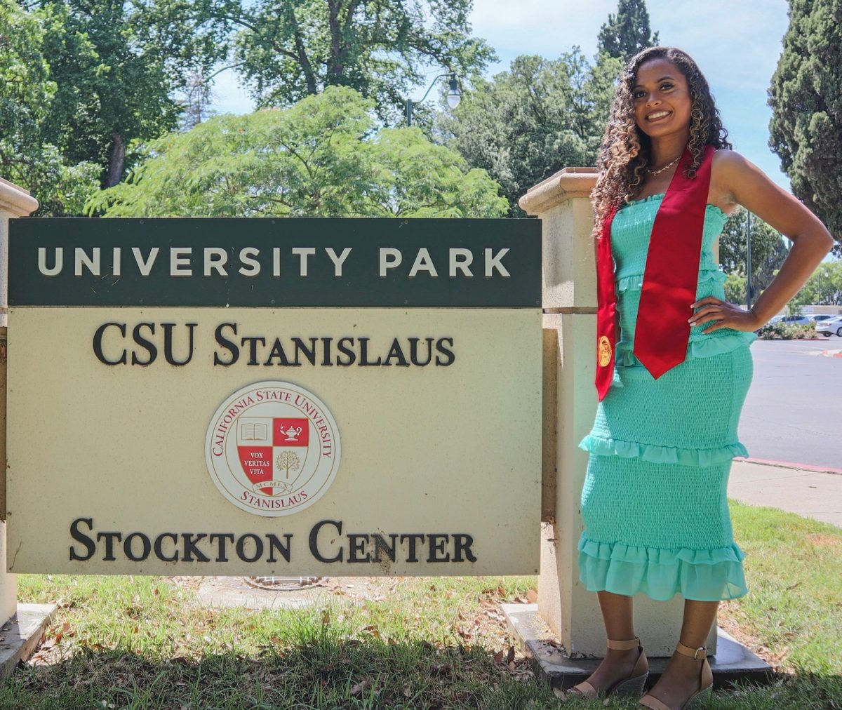 Aliyah Stoeckl posing in front of the CSU Stanislaus University Park in Stockton in her graduation gear.