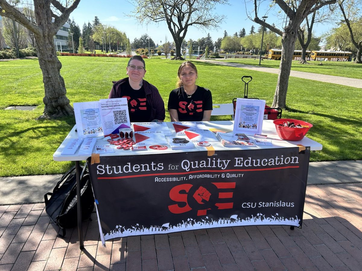 Shayla Garnica (Sophomore, Public Health Promotion) and Heather Oram (Senior, Sociology with a minor in Gender Studies) sitting at a table promoting their upcoming event in the quad on Monday, March 16, 2026, in Turlock.