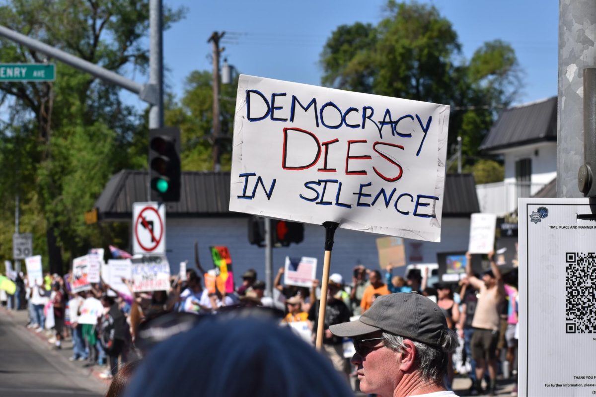 Protestors on 5 points chant, one sign reads, "Democracy dies in silence," on Saturday, March 28,  2026 at the No Kings Protest in Modesto.