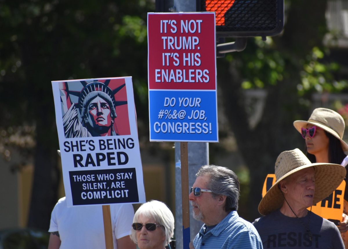 Two protestors holding up signs at ton Saturday, March 28,  2026 at the No Kings Protest in Modesto.